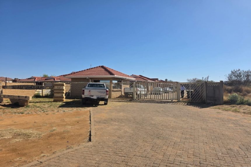 Gated house with parked bakkie in dry landscape.