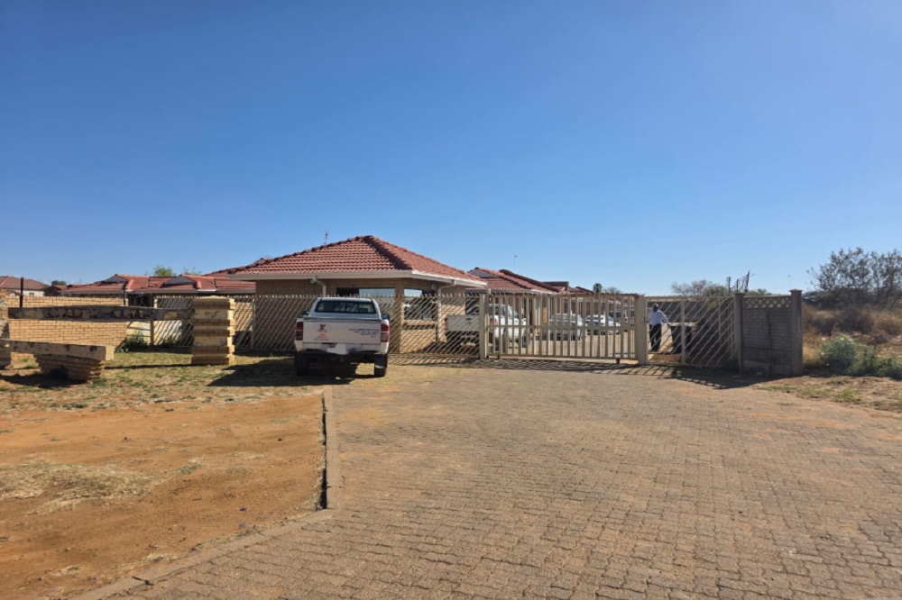Gated house with parked bakkie in dry landscape.