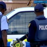 Two South African policemen standing by police vehicle.