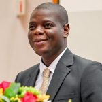 Man in suit with flowers, speaking confidently.