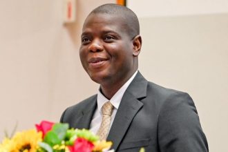 Man in suit with flowers, speaking confidently.