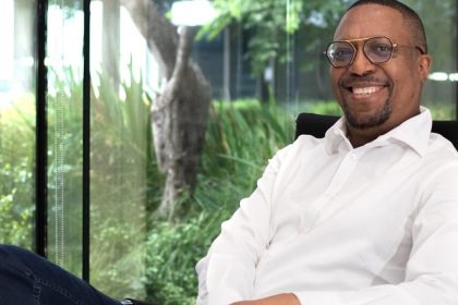 Smiling person sitting in office with greenery outside.