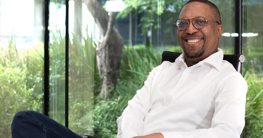 Smiling person sitting in office with greenery outside.