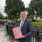 Man holding red cover document outdoors.
