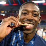 Footballer celebrates with gold medal on field.