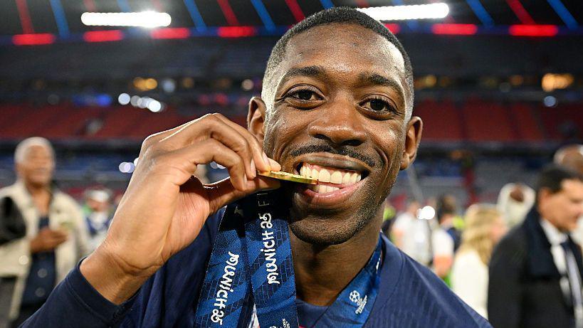 Footballer celebrates with gold medal on field.