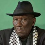 Person in black hat and patterned scarf, green background.