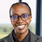 Person smiling, wearing glasses, grey suit indoors.