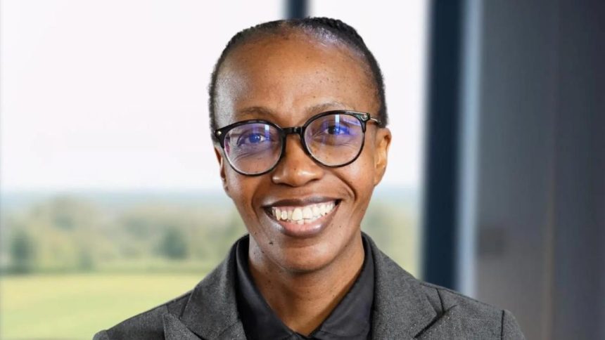 Person smiling, wearing glasses, grey suit indoors.