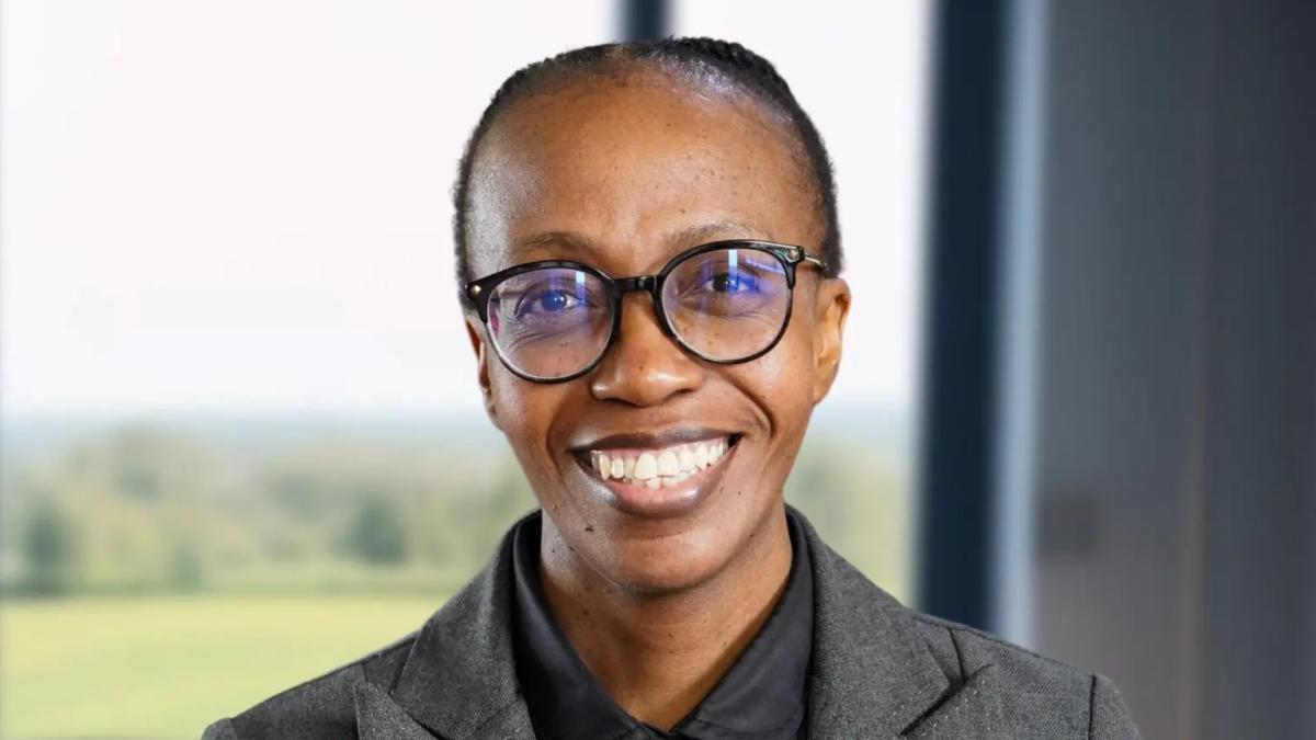 Person smiling, wearing glasses, grey suit indoors.
