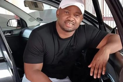 Man sitting in car, smiling and wearing cap.