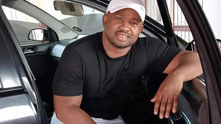 Man sitting in car, smiling and wearing cap.