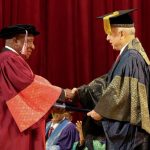 Graduation ceremony: handshake between officials on stage.