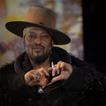 Person with hat making heart gesture.