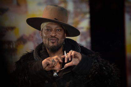 Person with hat making heart gesture.