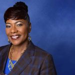 Smiling woman in blue background, professional attire.