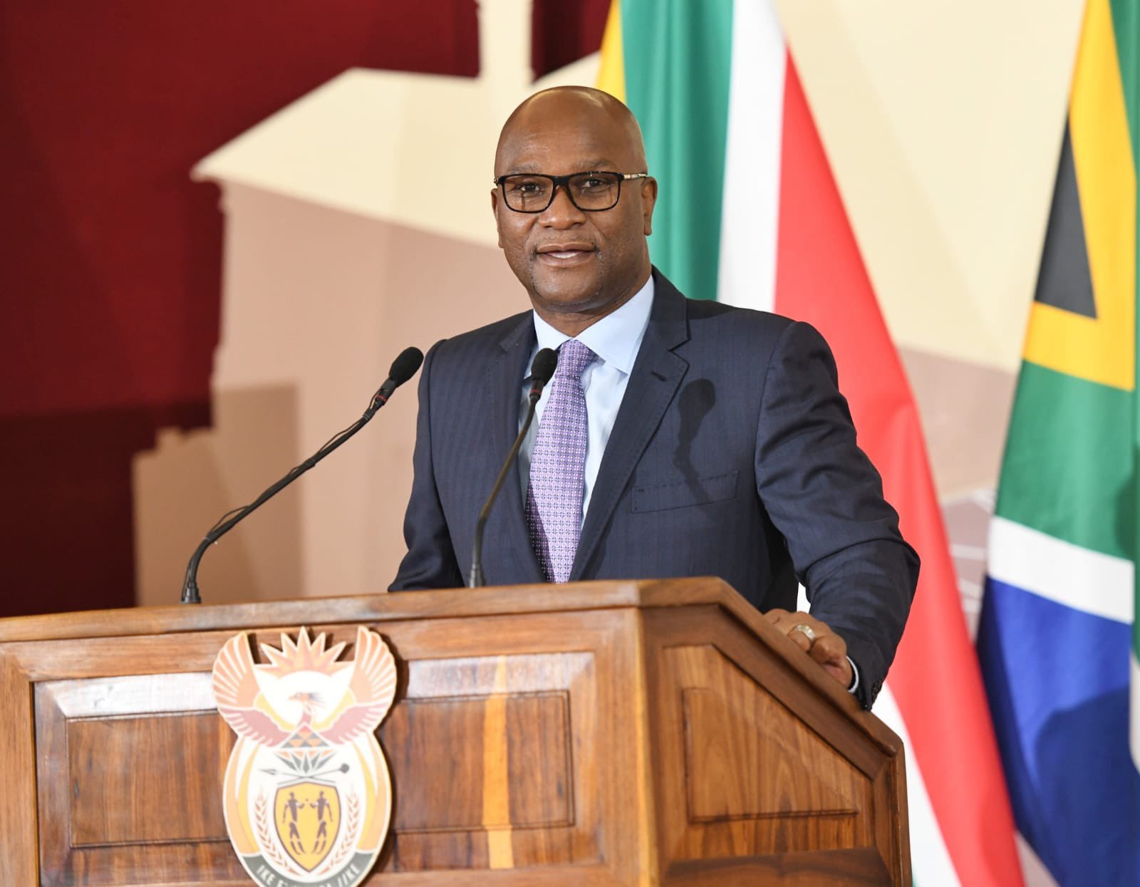 Man speaking at a podium with South African flag.