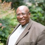 Smiling person in garden setting, wearing glasses.