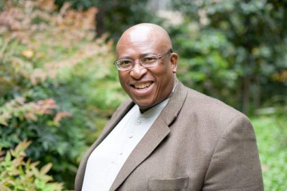 Smiling person in garden setting, wearing glasses.