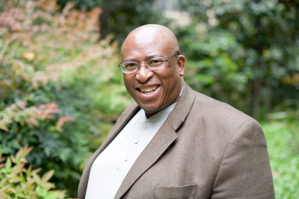 Smiling person in garden setting, wearing glasses.