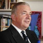 Smiling man in formal suit with bookshelf background.