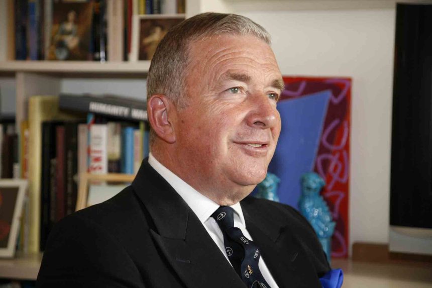 Smiling man in formal suit with bookshelf background.