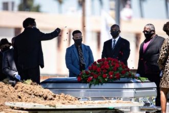 Funeral ceremony with mourners by a casket.