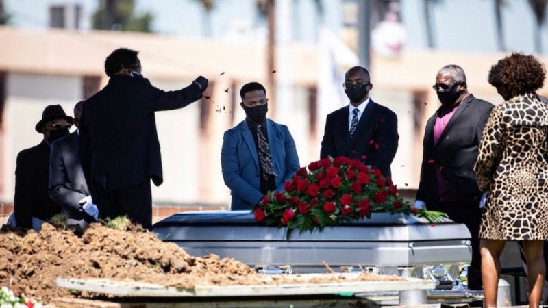 Funeral ceremony with mourners by a casket.