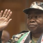 Person in camo outfit raising right hand.