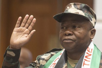 Person in camo outfit raising right hand.