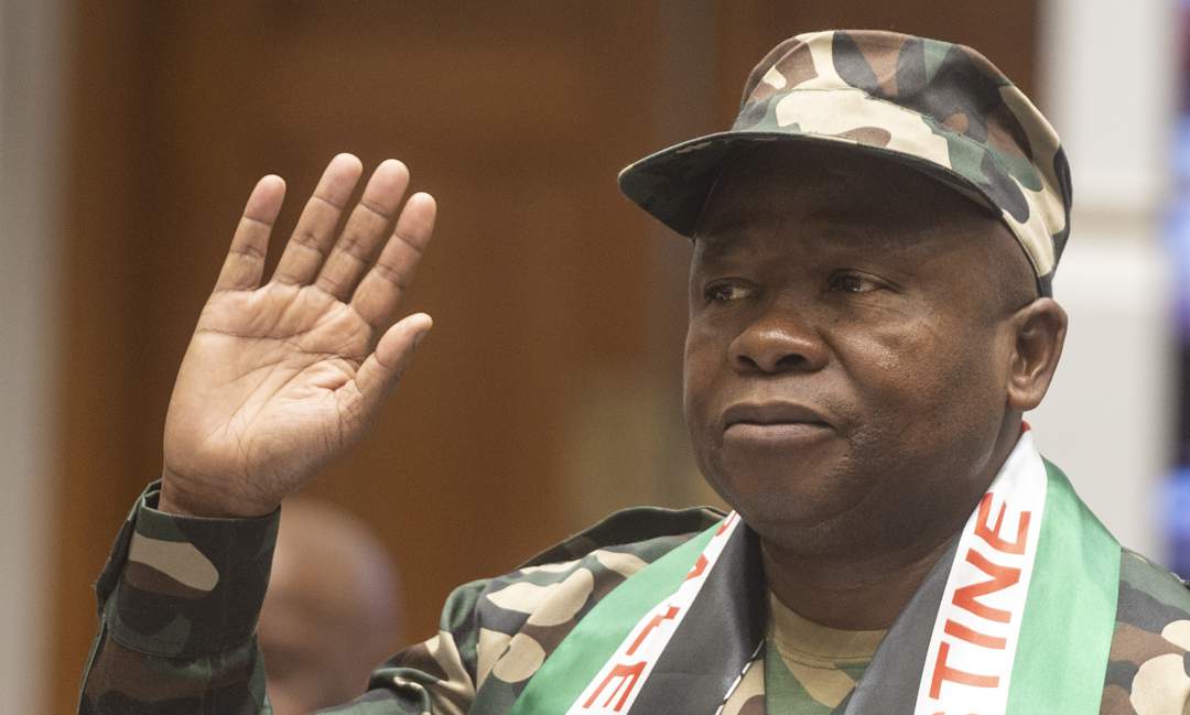 Person in camo outfit raising right hand.