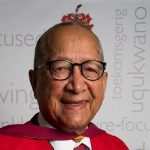 Elderly man in academic gown smiling.