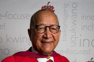 Elderly man in academic gown smiling.