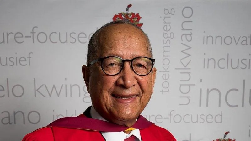 Elderly man in academic gown smiling.