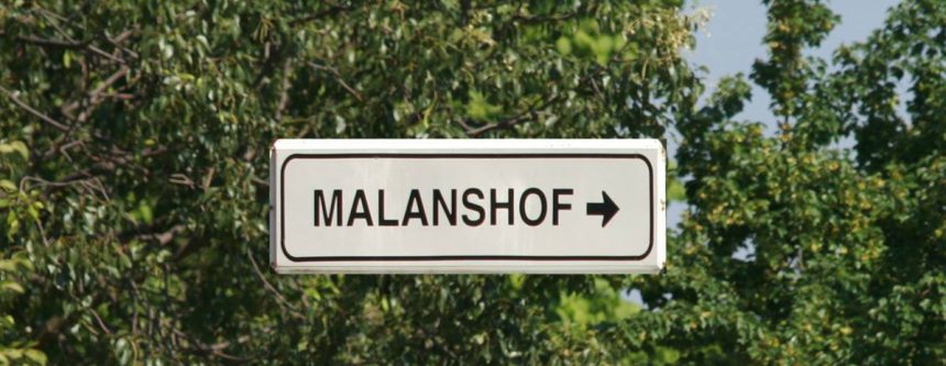 Sign pointing to Malanshof amid trees.