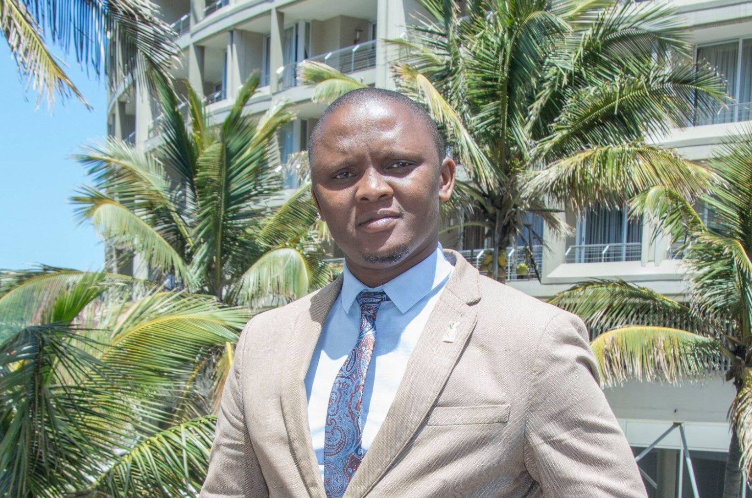 Man in suit, standing by palm trees and building