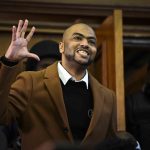 Man in coat smiling, raising hand in courtroom.