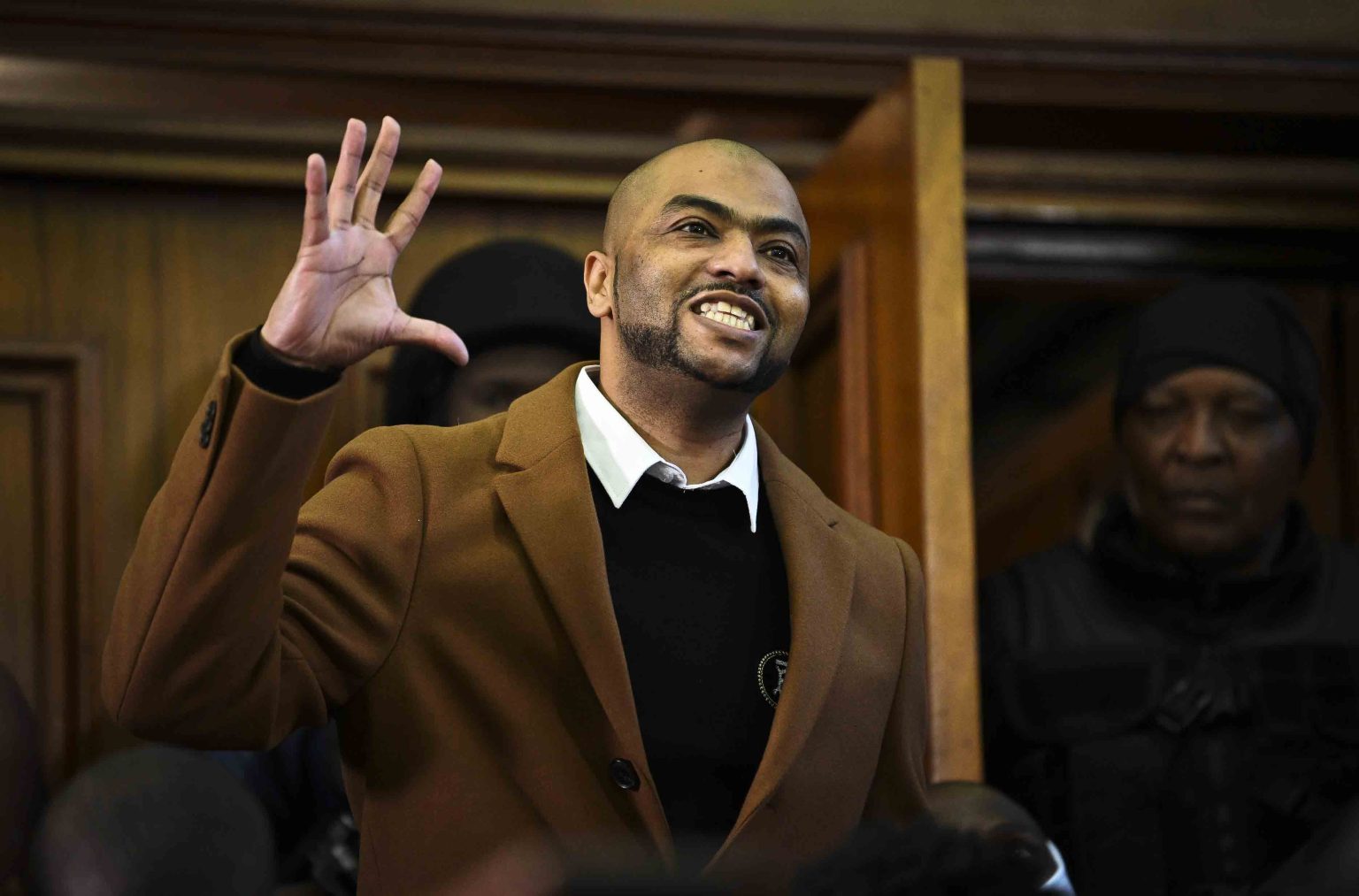 Man in coat smiling, raising hand in courtroom.