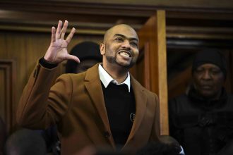 Man in coat smiling, raising hand in courtroom.