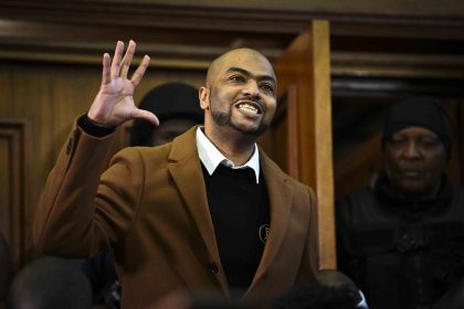 Man in coat smiling, raising hand in courtroom.