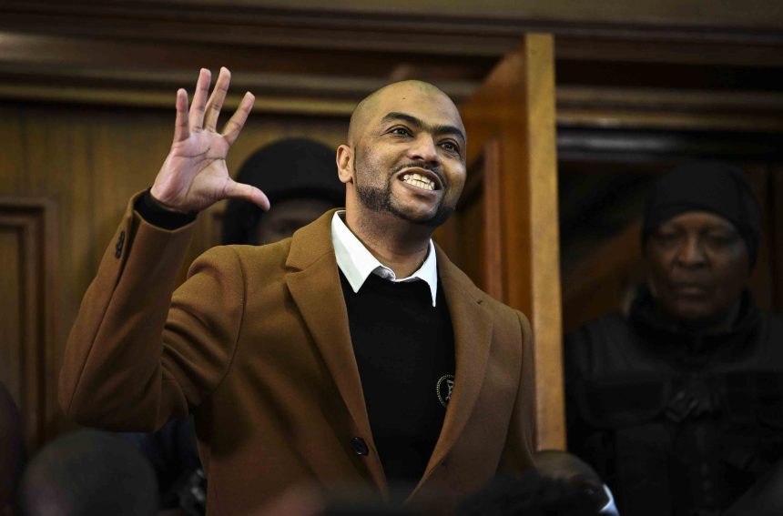 Man in coat smiling, raising hand in courtroom.
