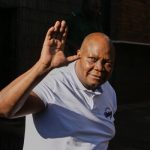 Man in white shirt waves outdoors.
