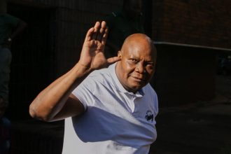 Man in white shirt waves outdoors.