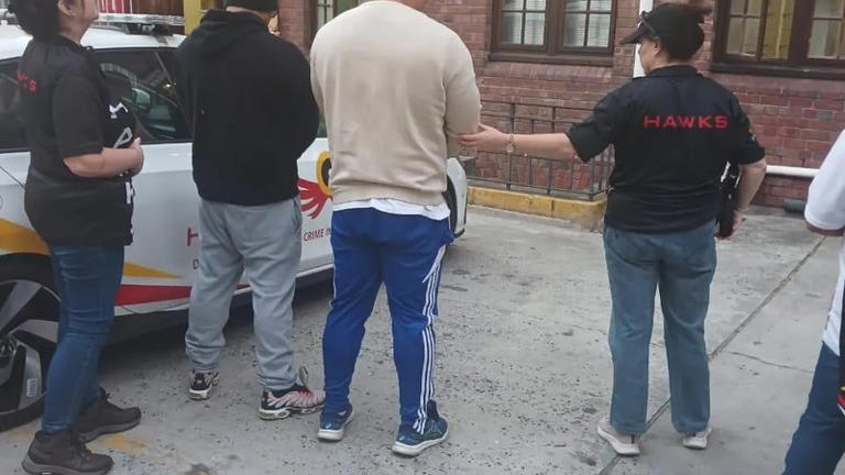 Hawks officers arrest suspects near an official vehicle.