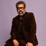 Man in brown suit posing against purple background