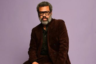 Man in brown suit posing against purple background