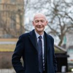 Smiling person in coat outdoors with building background.