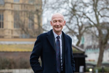 Smiling person in coat outdoors with building background.