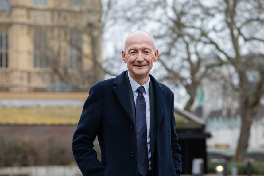 Smiling person in coat outdoors with building background.