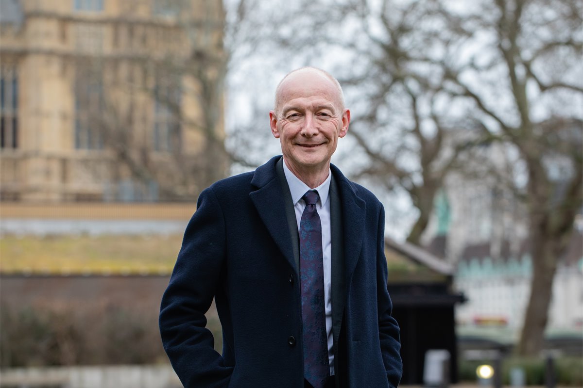 Smiling person in coat outdoors with building background.